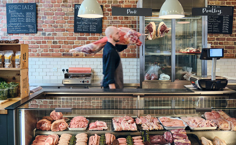 Meat counter at Ruby & White butchers with person carrying large piece of meat in the background